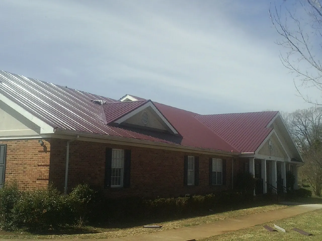 Red metal roof with gabled entries on a long brick building, from a Hail Damage Roof Repair job in Geneva